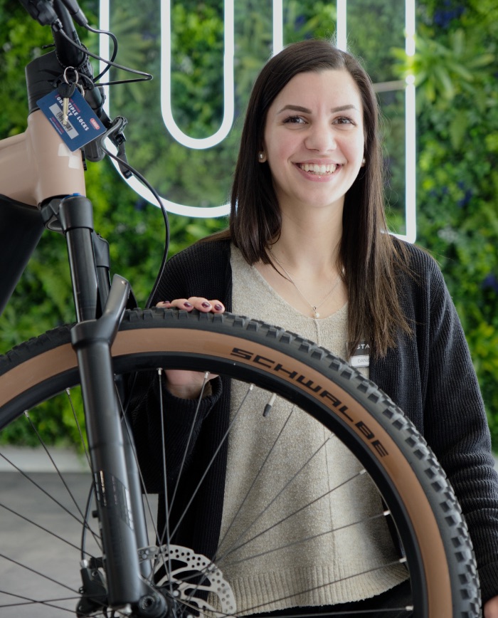 Mitarbeiterin lächelt neben einem Fahrrad mit Schwalbe-Reifen – moderner Showroom mit Pflanzenwand im Hintergrund.